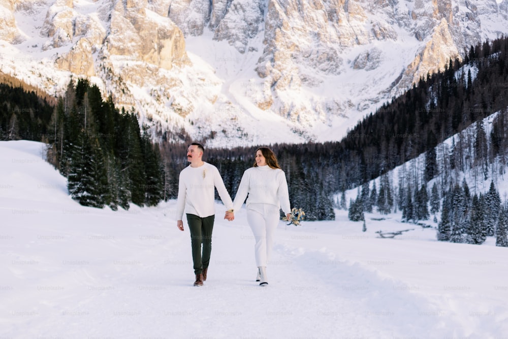 Ein Mann und eine Frau, die Händchen haltend im Schnee spazieren gehen