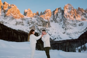 a man and woman standing in the snow with mountains in the background