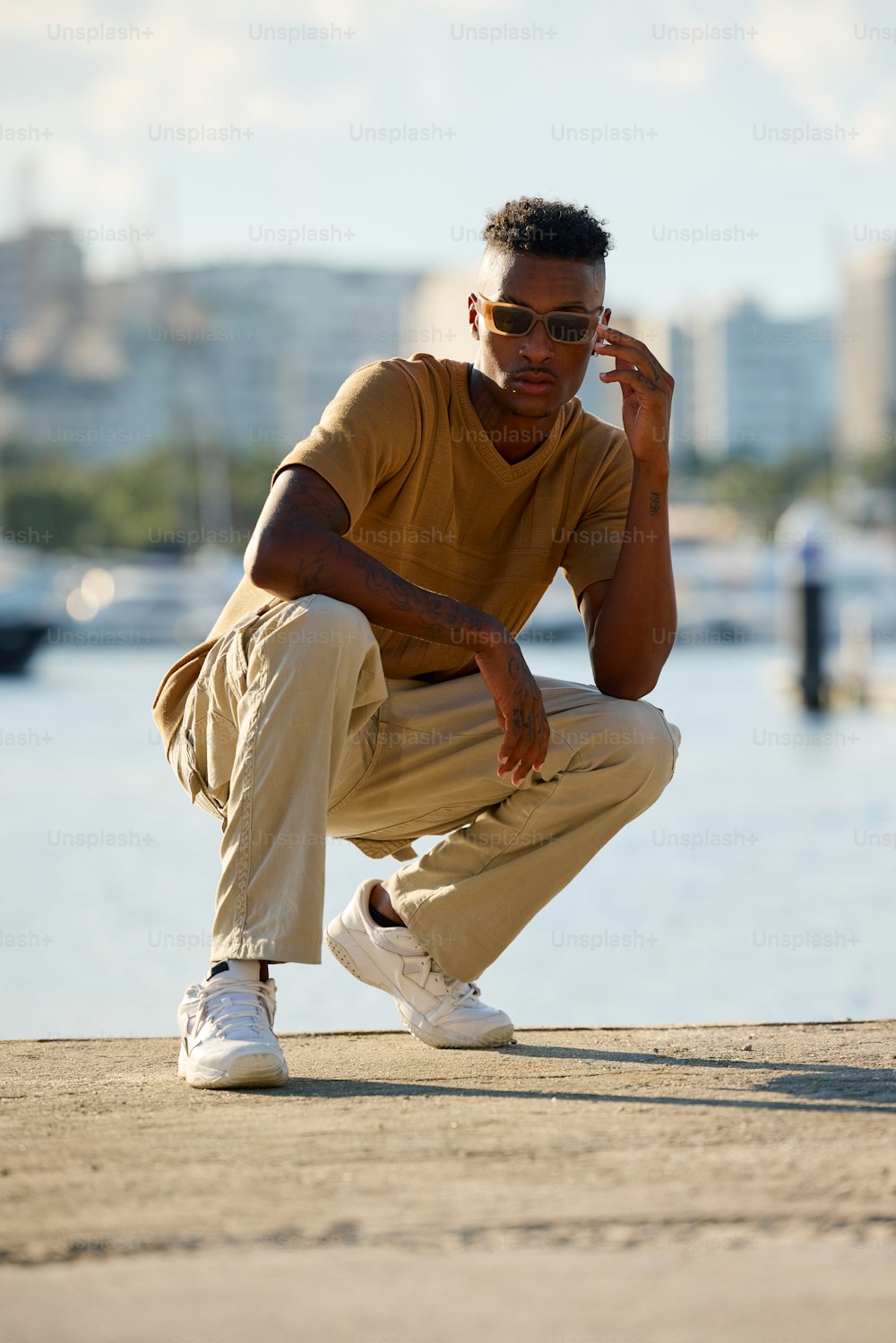 a man in a tan shirt and khaki pants squatting on a dock