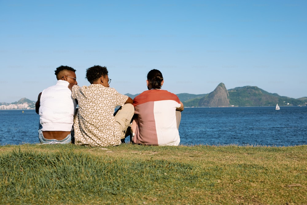 três pessoas sentadas em uma colina com vista para um corpo de água
