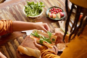 two people are preparing sandwiches on a wooden table