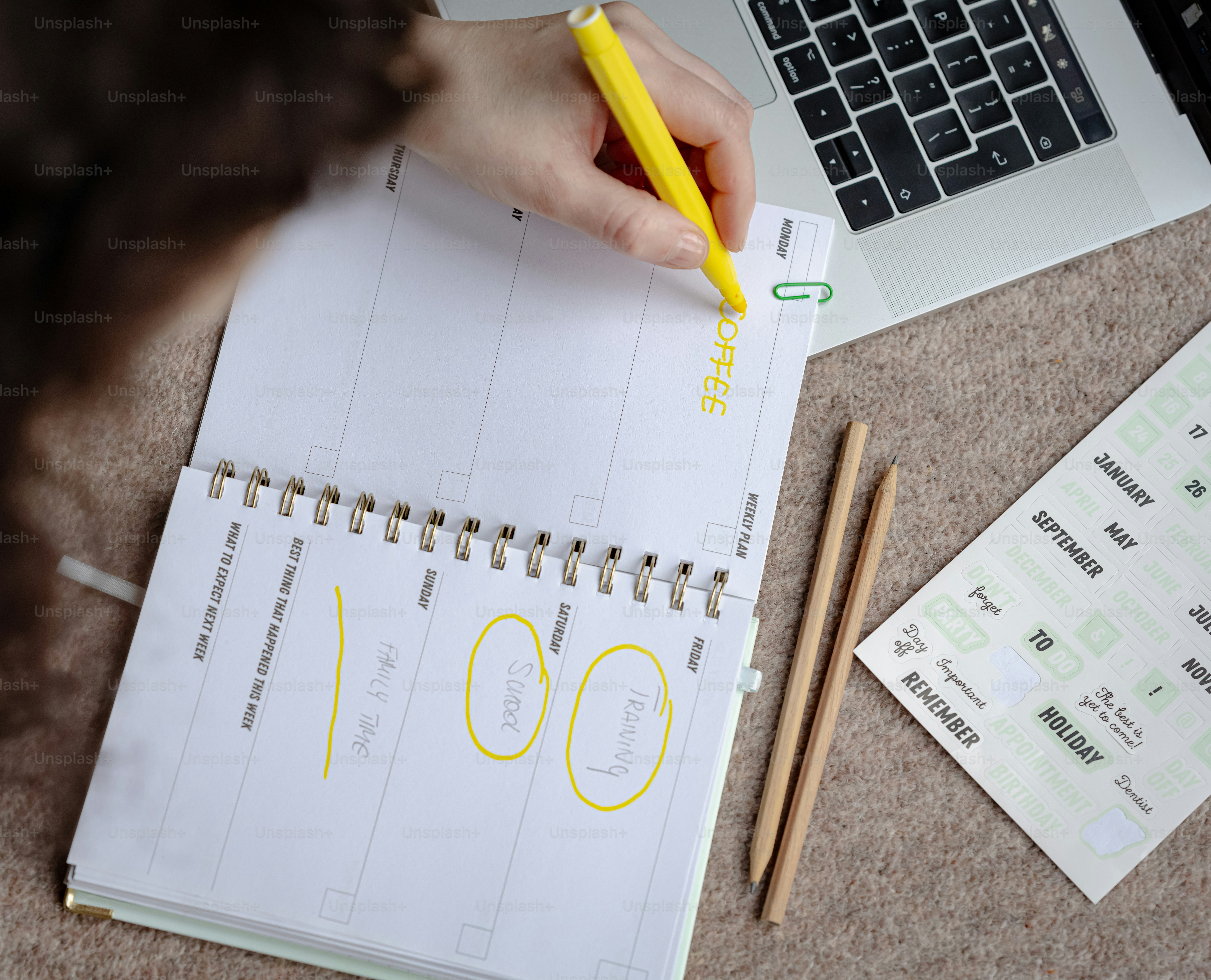 a person writing on a notebook next to a laptop