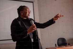 a woman speaking into a microphone in front of a projector screen