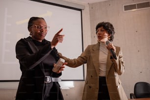 two women standing next to each other in front of a projector screen
