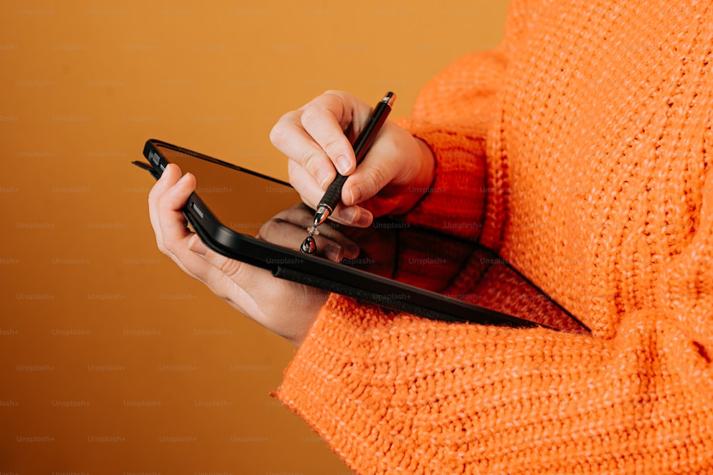 주황색 스웨터를 입은 여성이 휴대전화를 들고 있다
