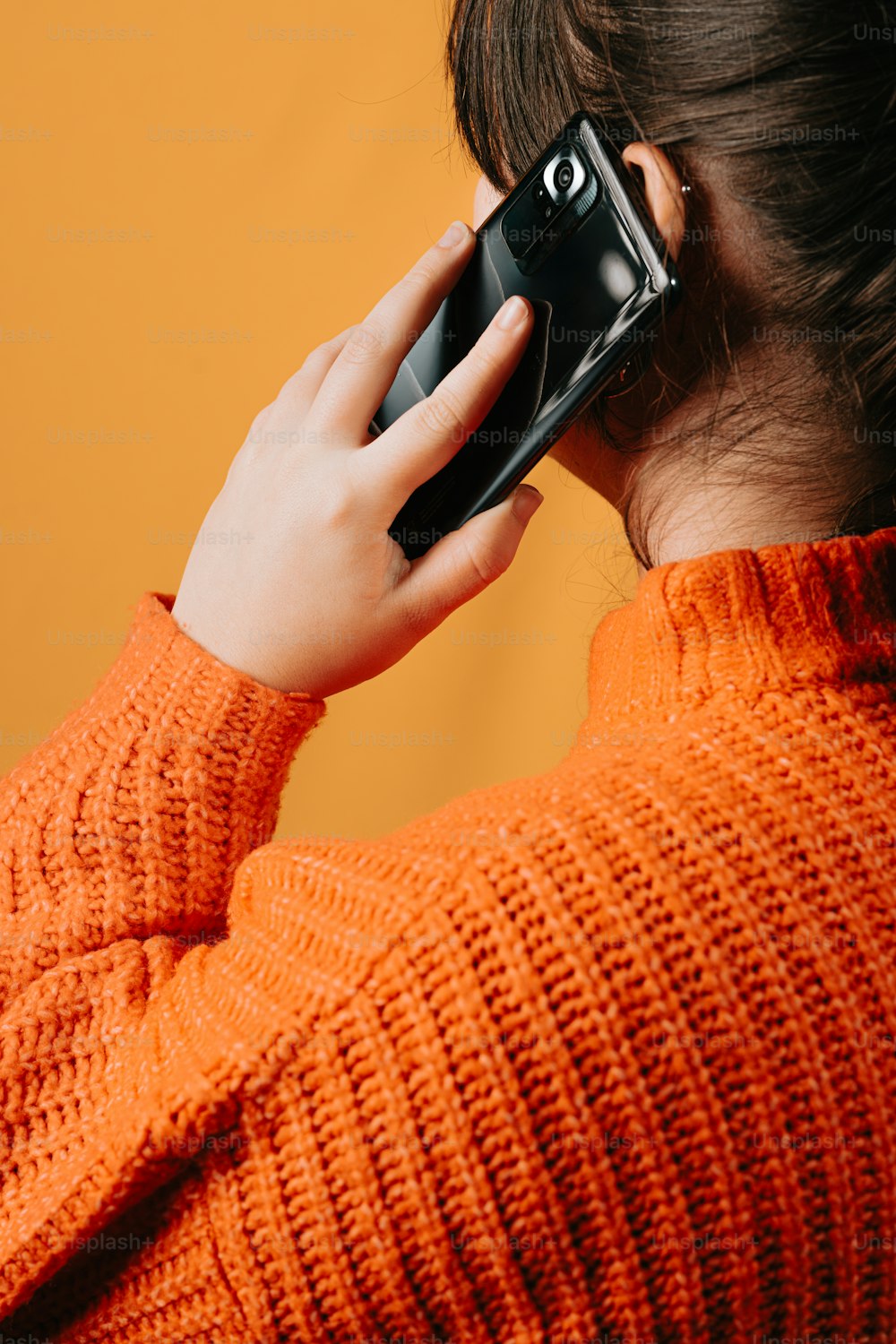 a woman in an orange sweater talking on a cell phone