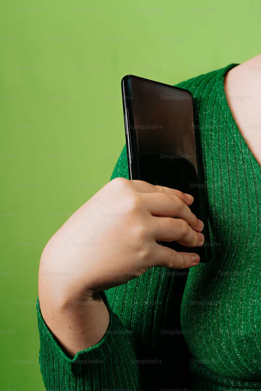 una donna in un maglione verde che tiene in mano un telefono cellulare