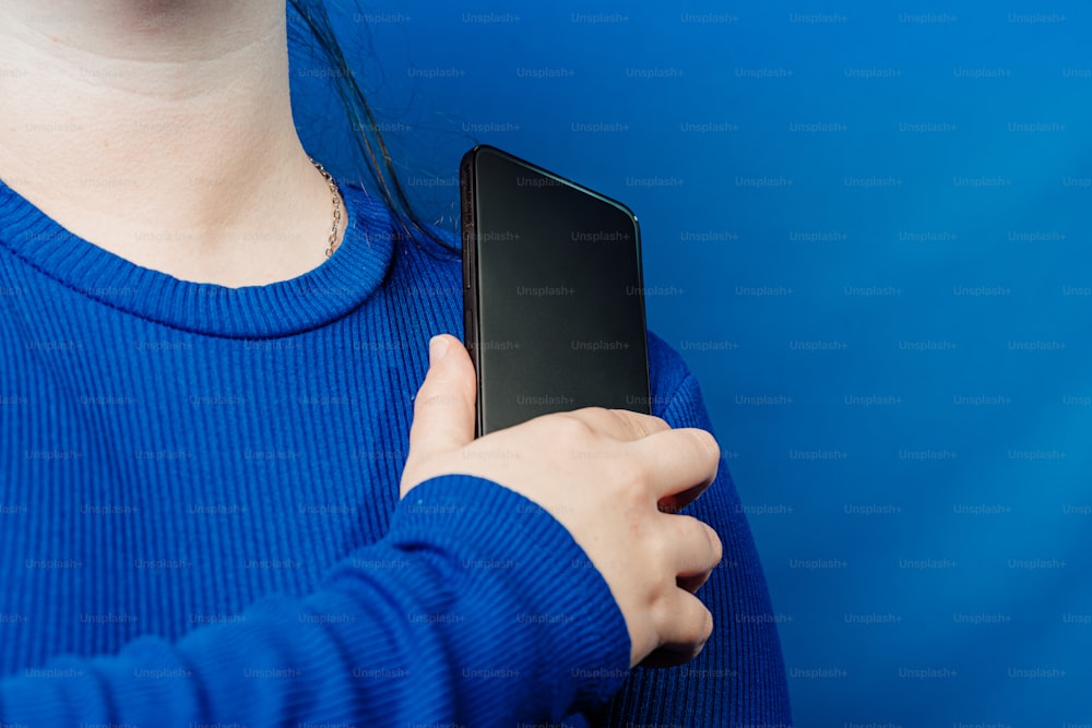 una donna in un maglione blu che tiene in mano un telefono cellulare