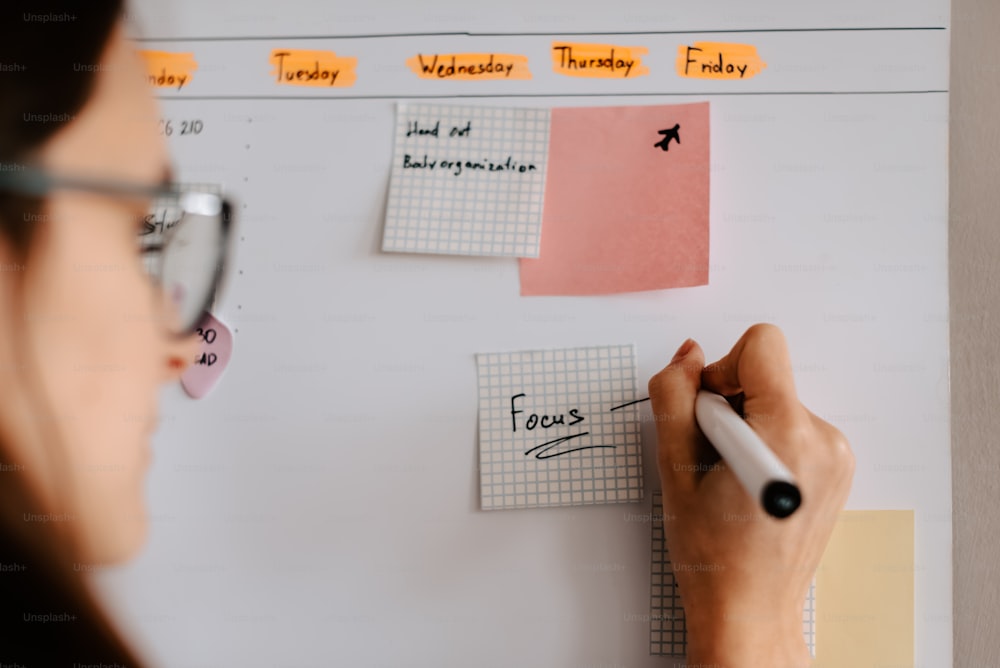 a woman writing on a white board with sticky notes