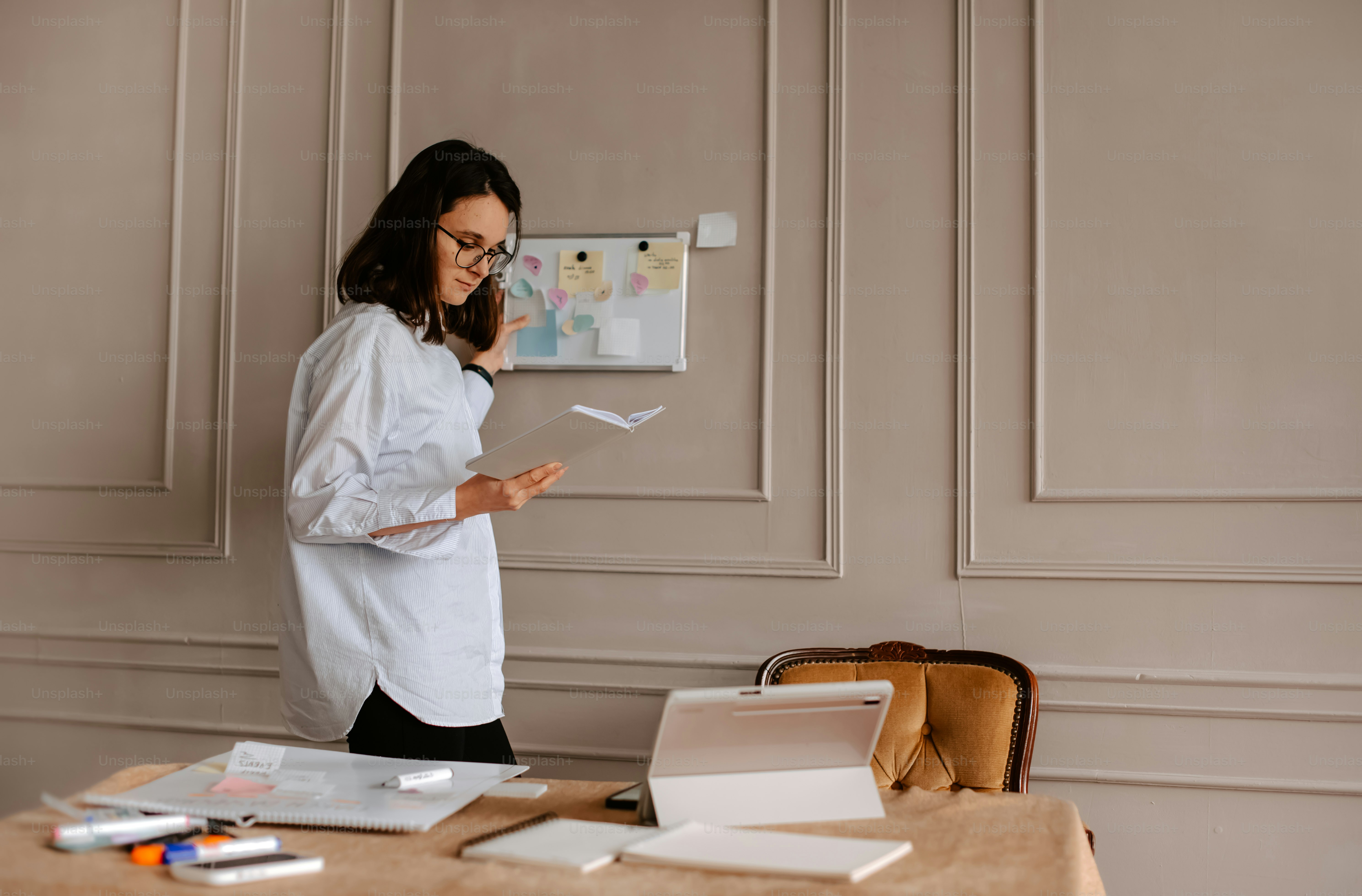 a woman standing in front of a desk holding a piece of paper