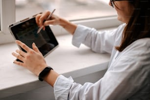 a woman sitting at a window sill using a tablet