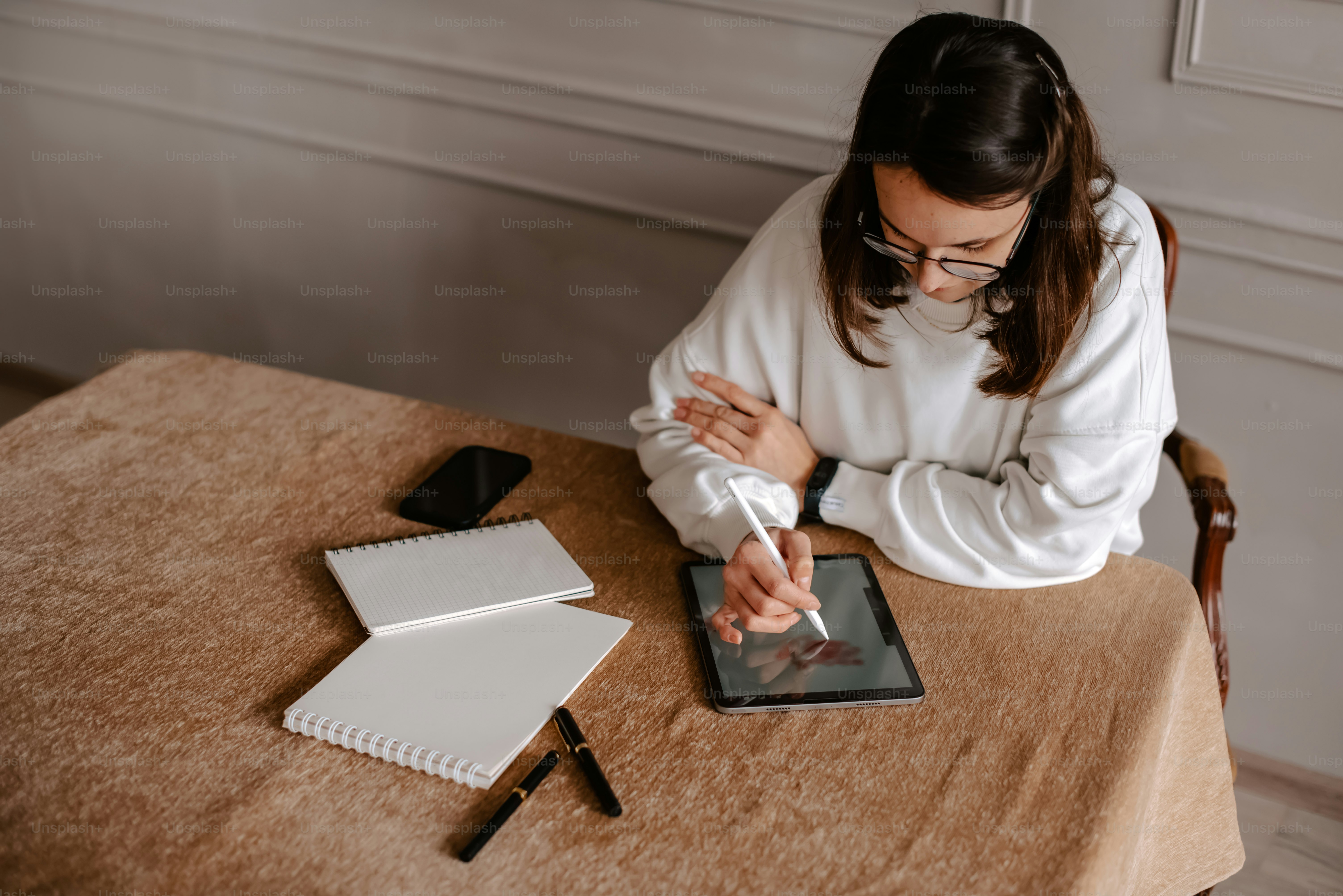 a woman sitting at a table writing on a tablet