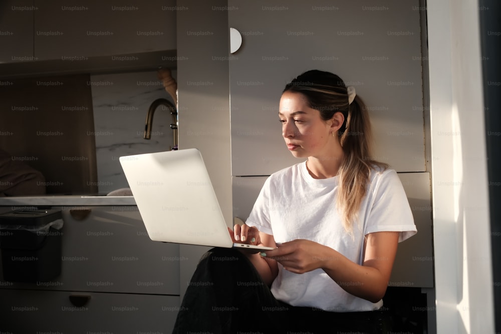 a woman sitting in a kitchen using a laptop computer