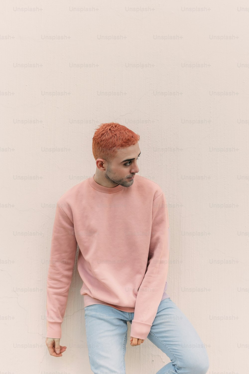 a man in a pink sweater leaning against a wall