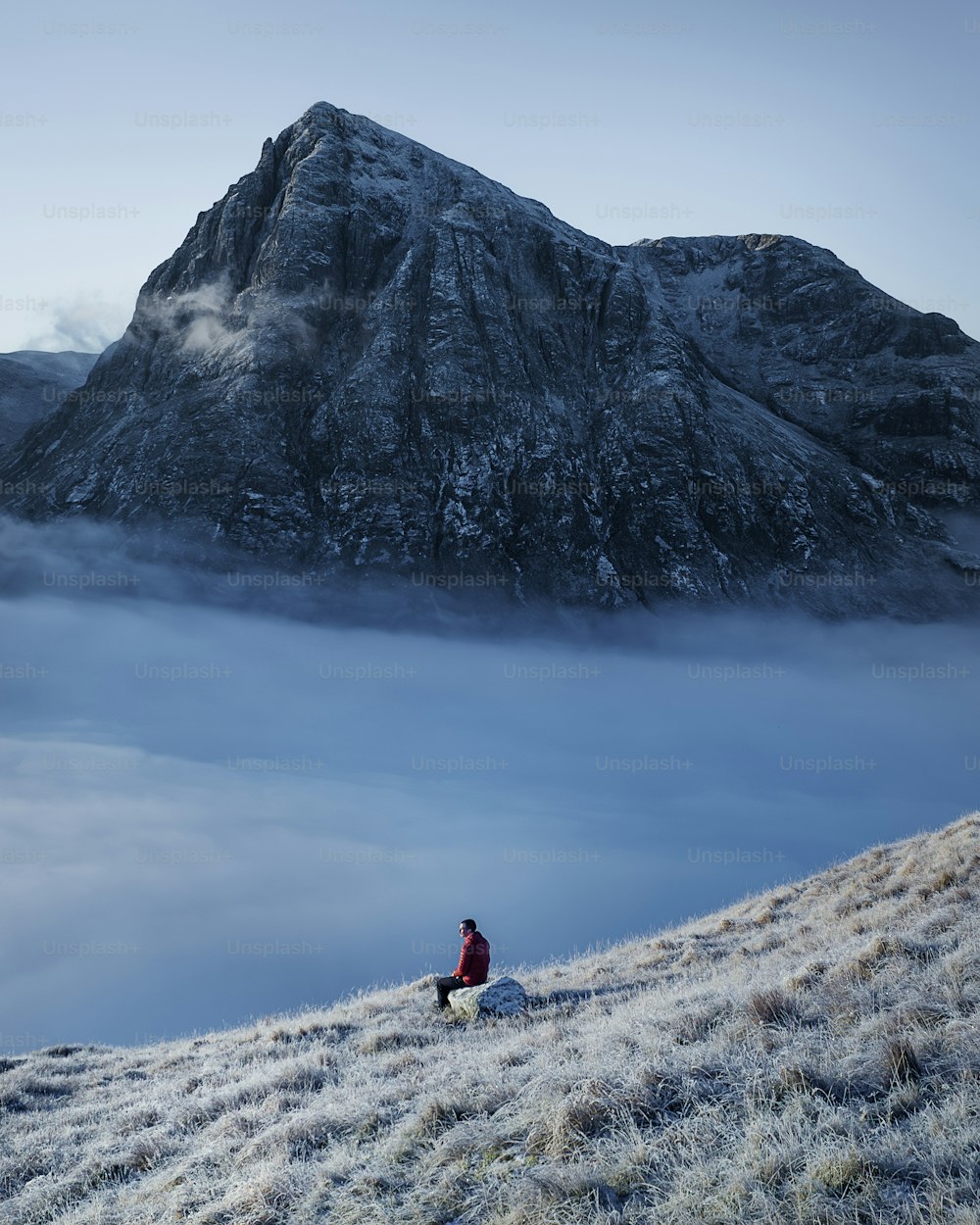 una persona seduta su una collina con una montagna sullo sfondo