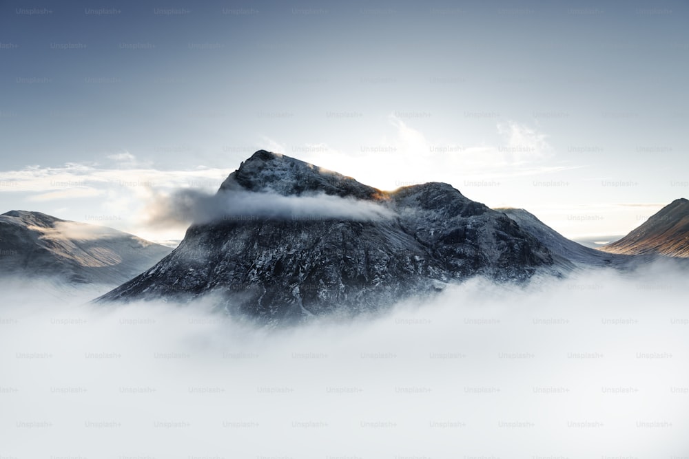 a mountain covered in fog and clouds under a blue sky