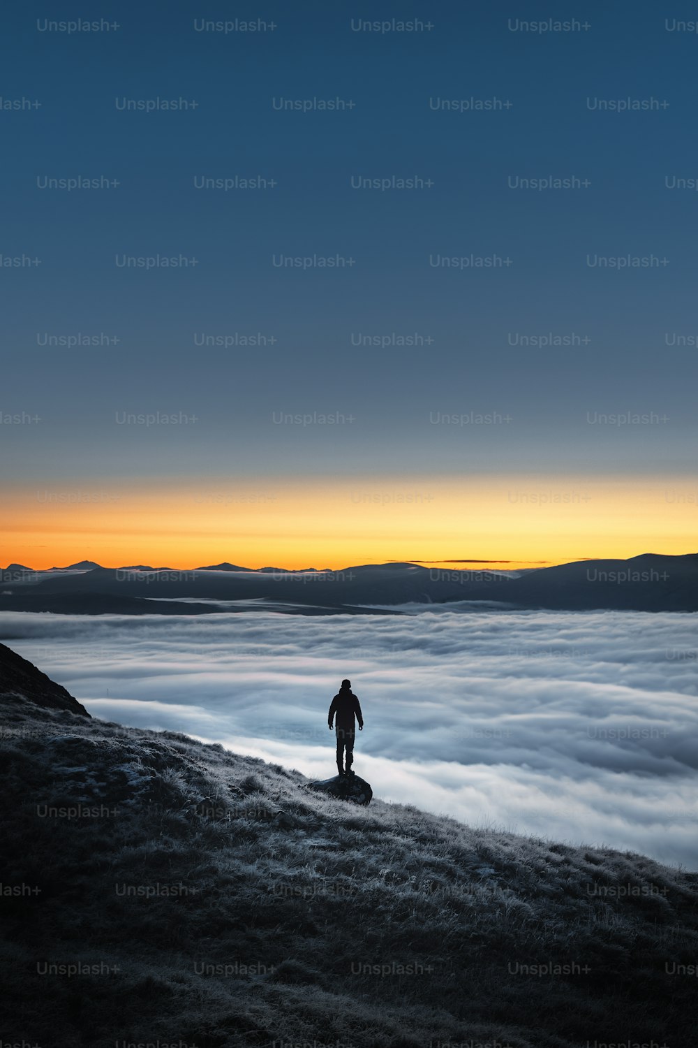 une personne debout au sommet d’une colline au-dessus des nuages