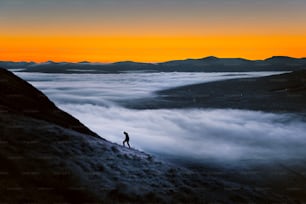 una persona in piedi sulla cima di una montagna circondata da nuvole