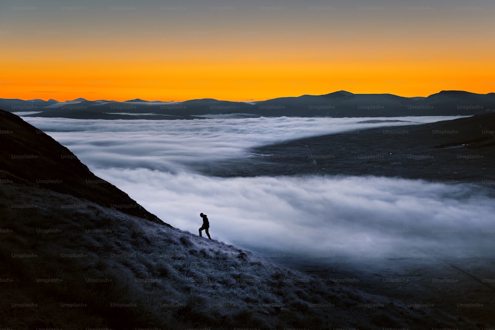 una persona de pie en la cima de una montaña rodeada de nubes