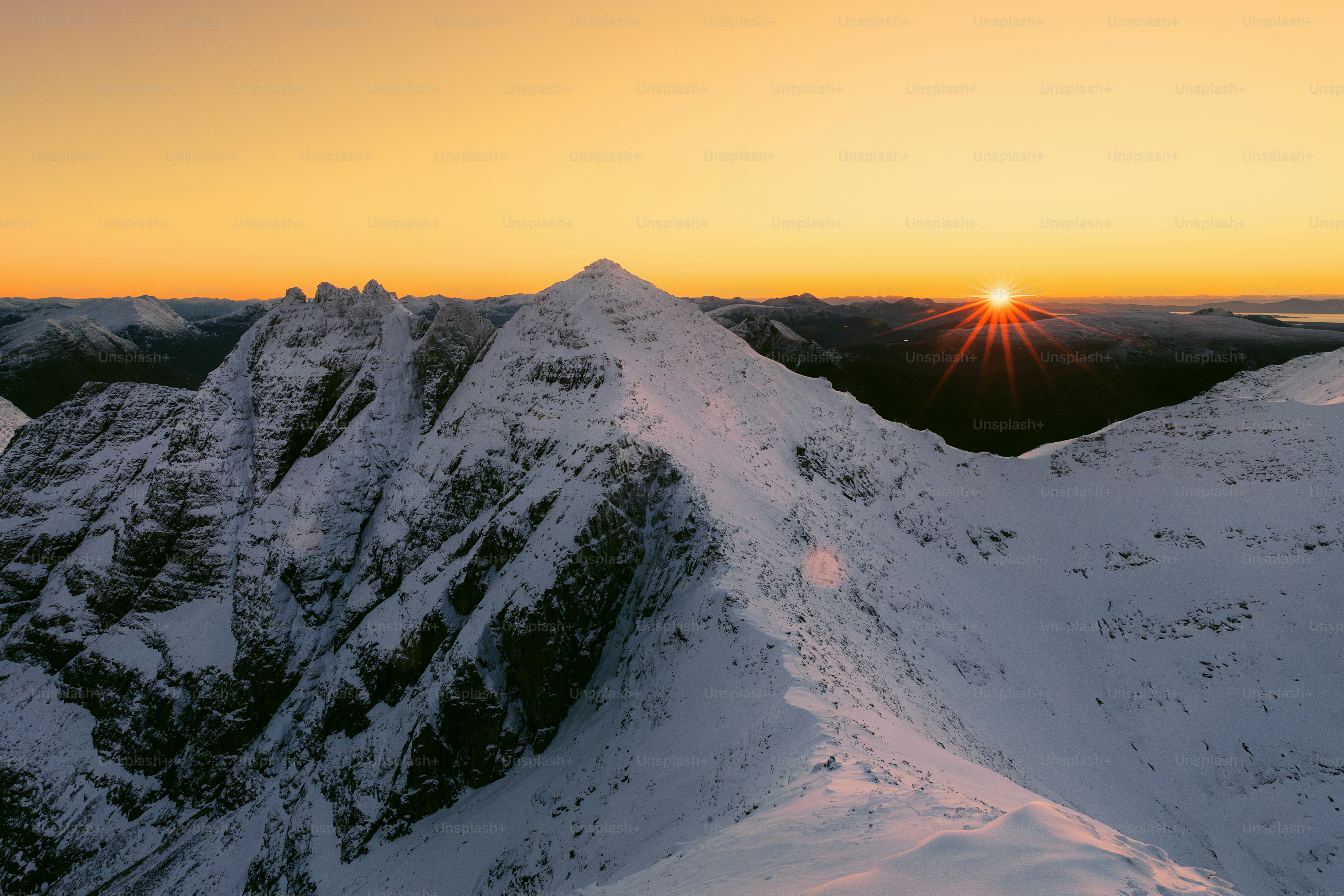 the sun is setting over a snowy mountain range