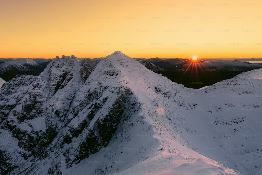 the sun is setting over a snowy mountain range