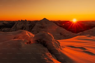 the sun is setting over a snowy mountain range