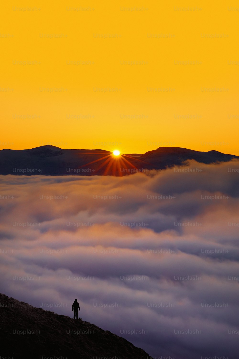 una persona de pie en la cima de una colina con una puesta de sol en el fondo