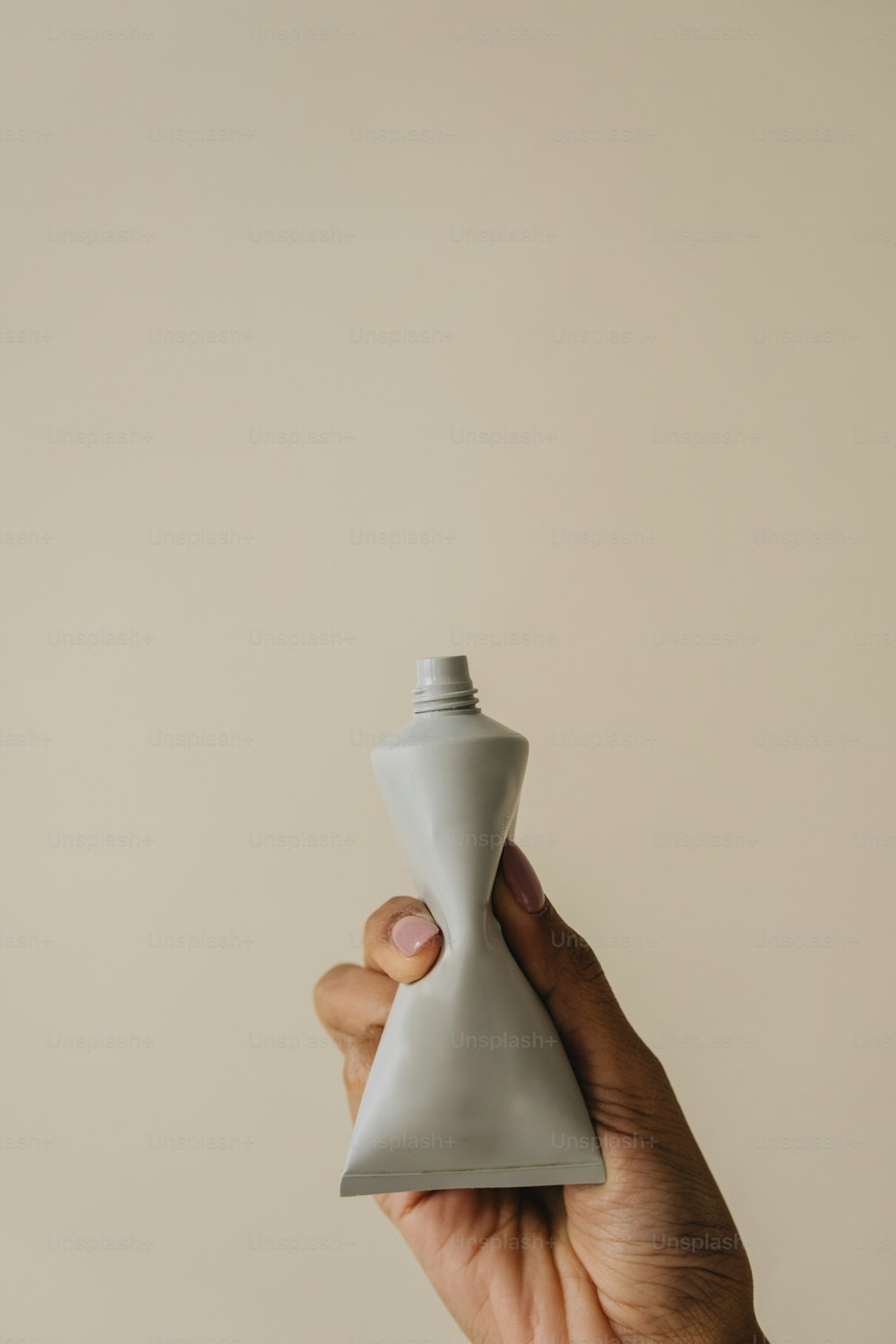 a hand holding a gray bottle in front of a white wall