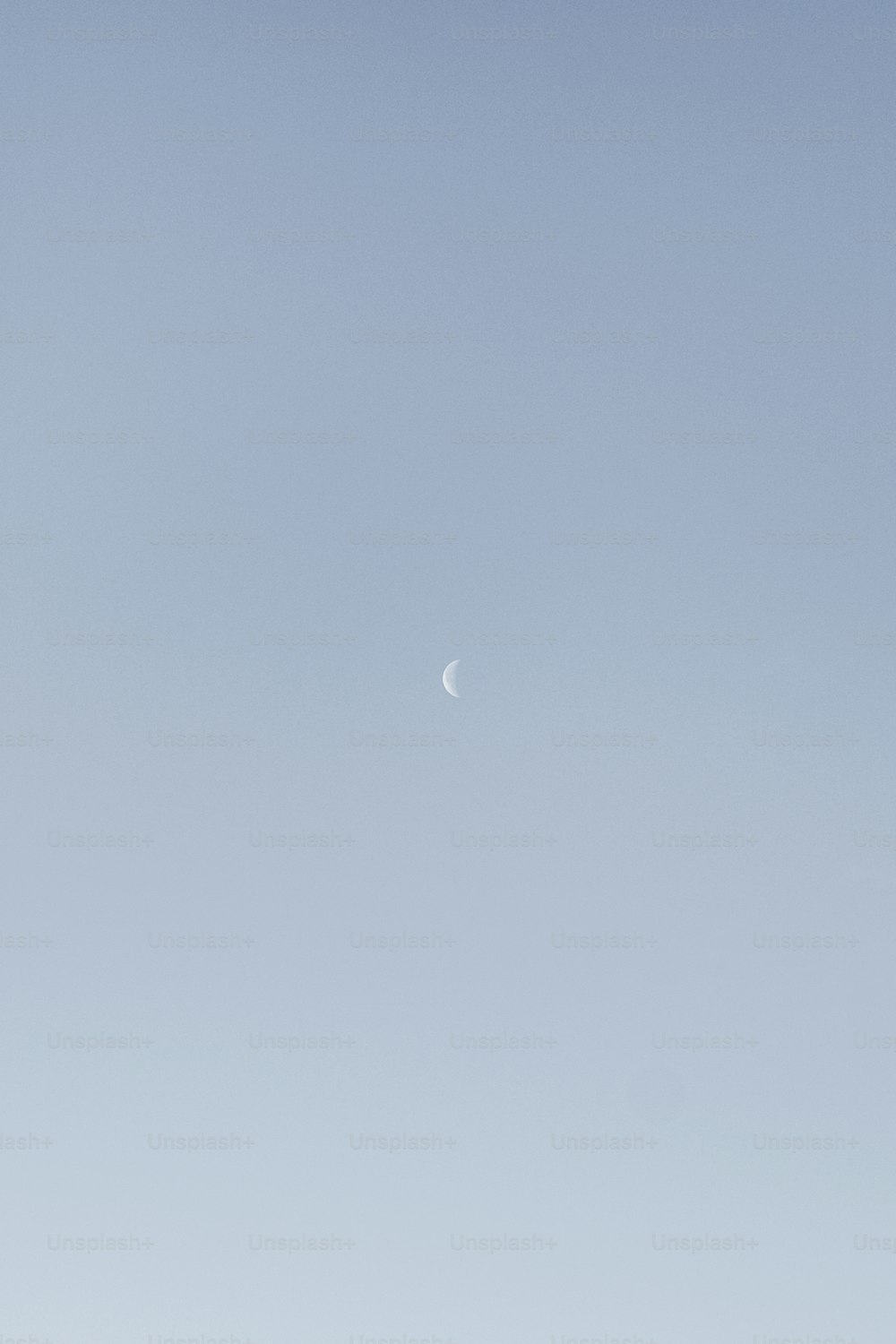 a plane flying in the sky with a half moon in the distance
