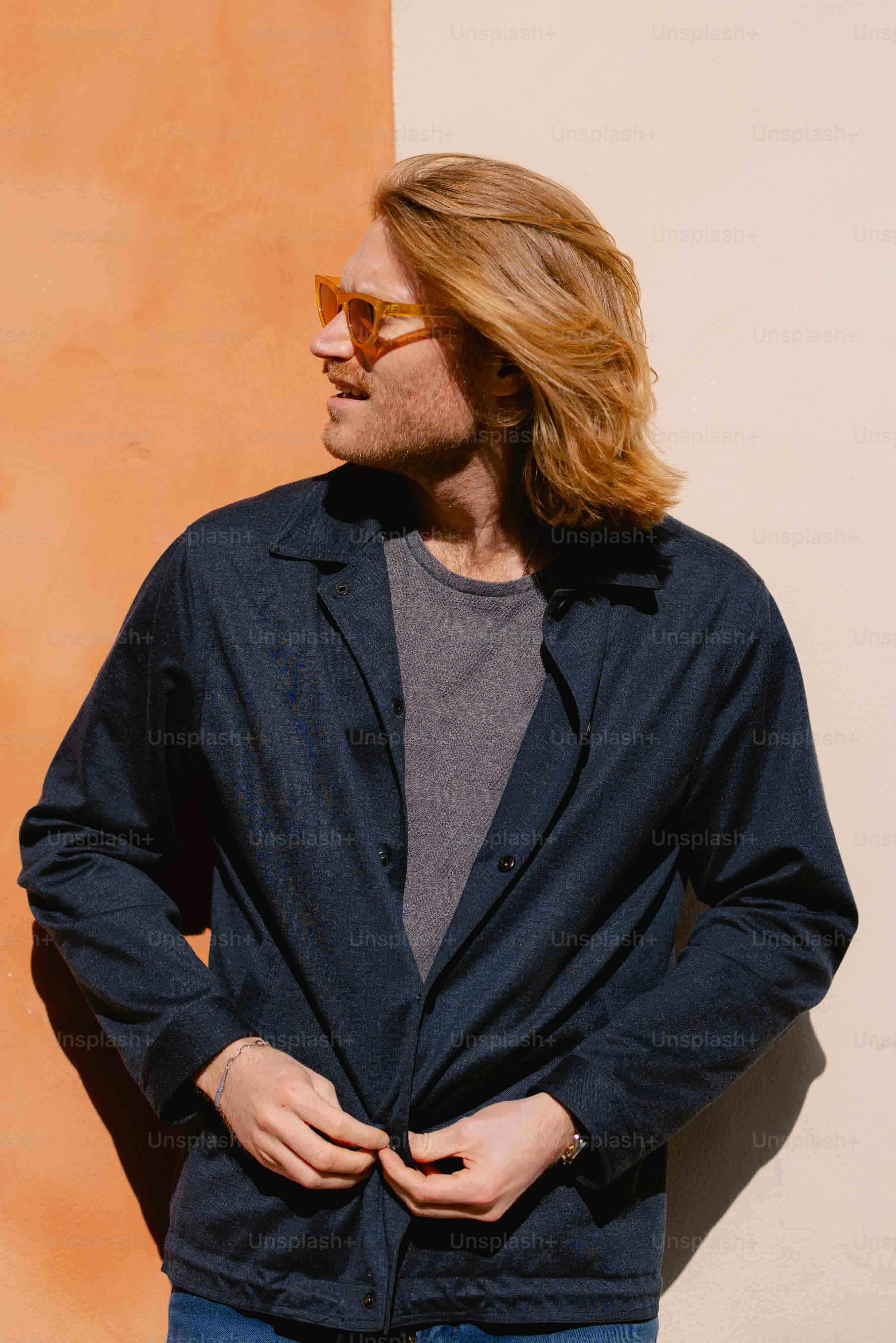 A man with long hair and sunglasses standing in front of a wall photo ...
