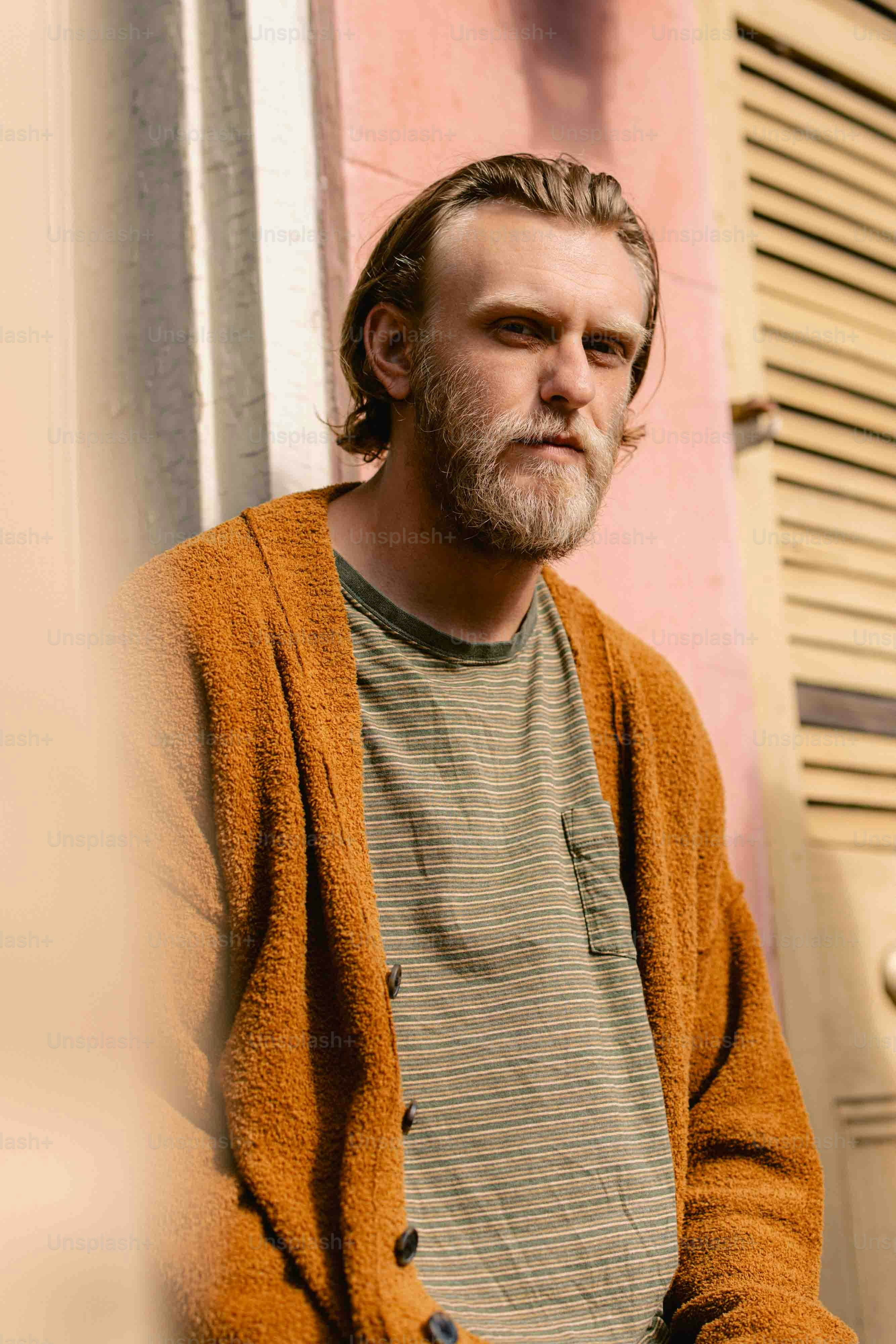 a man leaning against a wall wearing a brown cardigan