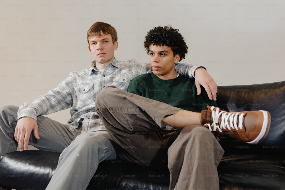 two young men sitting on a black leather couch