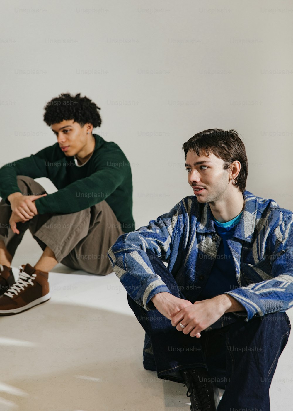 two young men sitting on the floor in front of a white wall