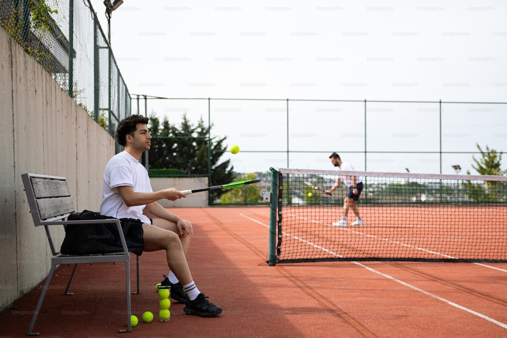 ein Mann sitzt auf einem Stuhl und hält einen Tennisschläger in der Hand