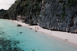 a couple of people walking along a beach next to a cliff