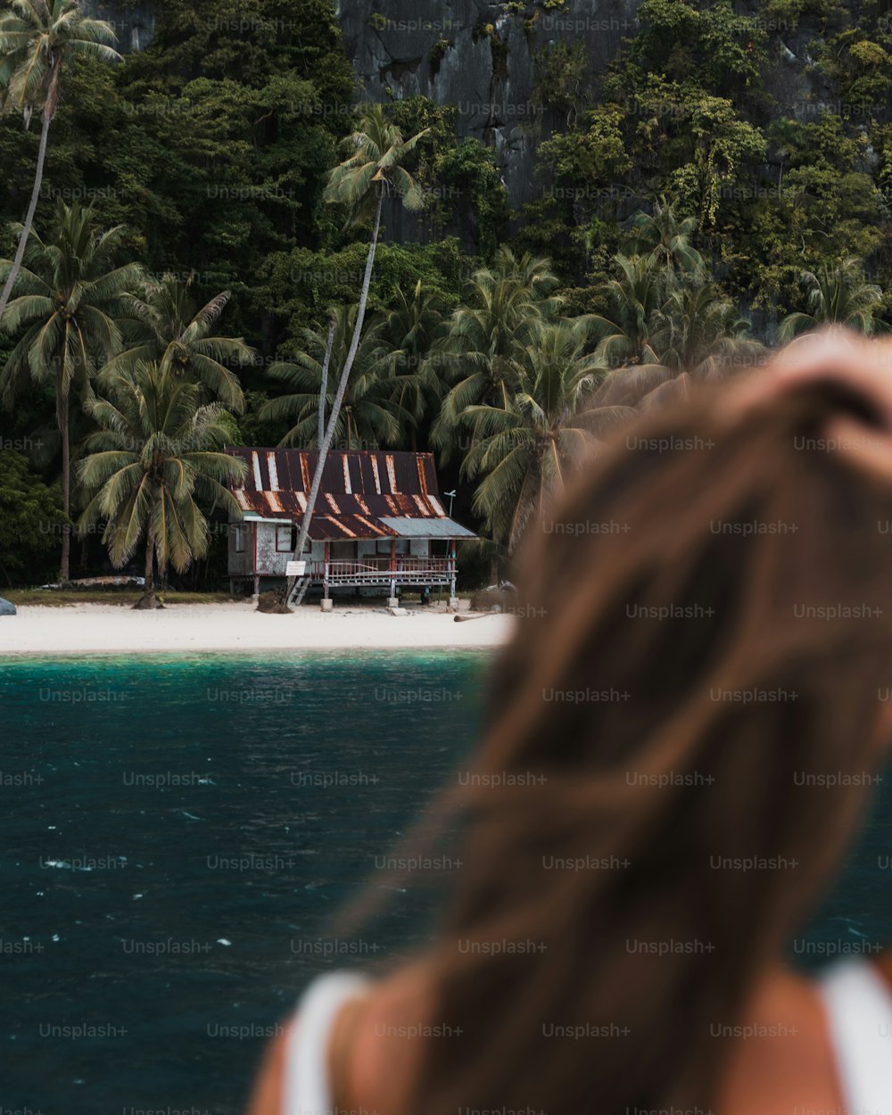 a woman standing on a beach looking at a house