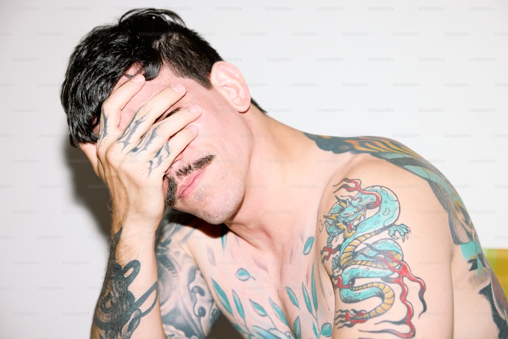 a man with tattoos covers his face with his hands
