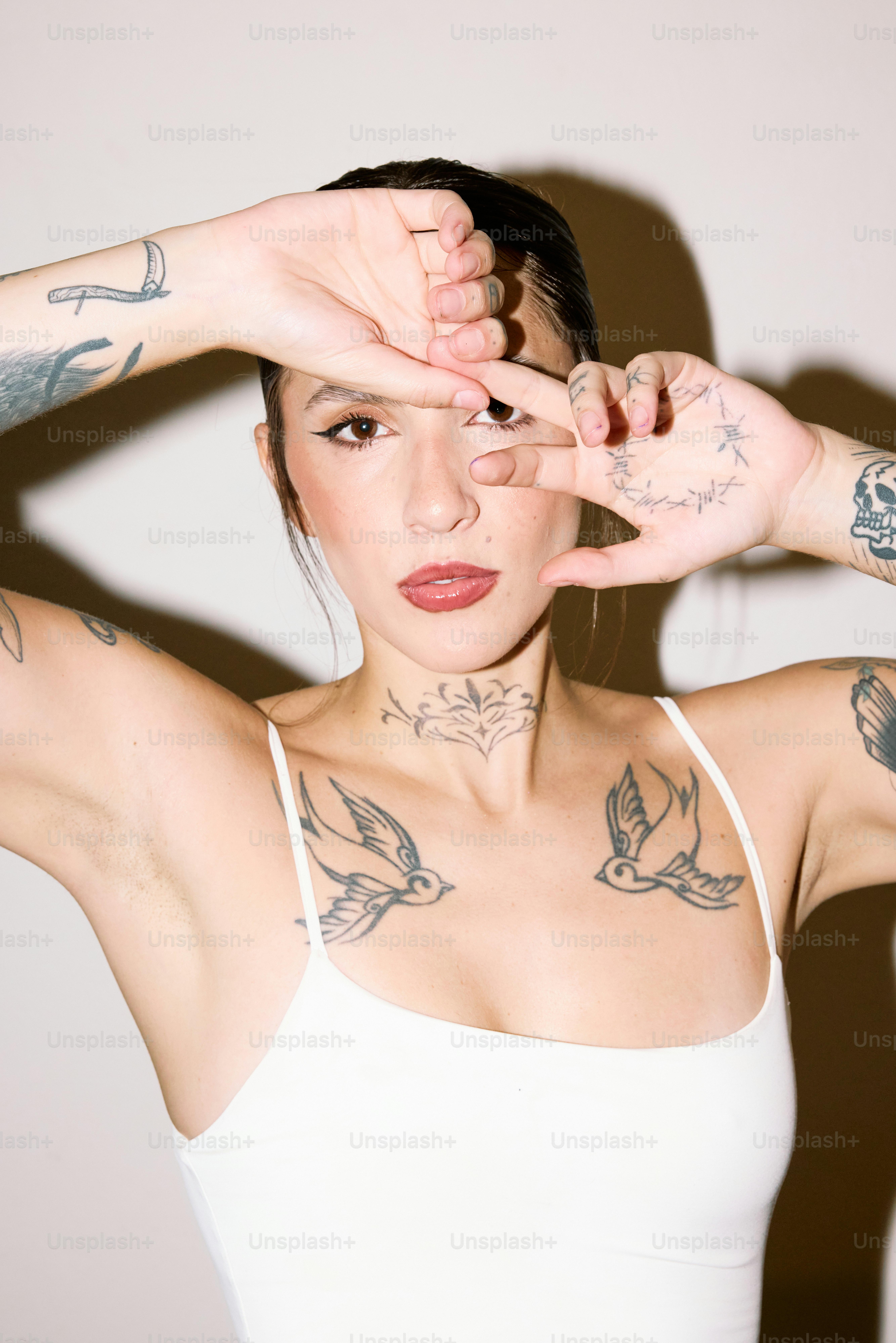 a woman in a white tank top holding her hands up to her face