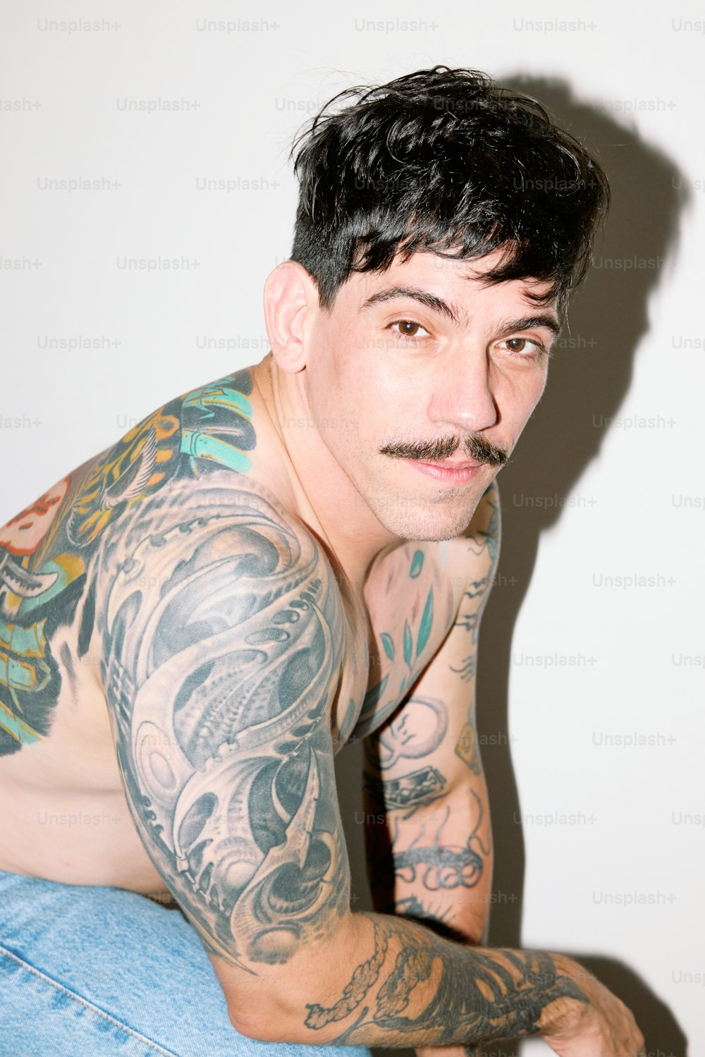 a man with tattoos and a moustache sitting down