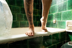 a person standing on a ledge in a green tiled bathroom