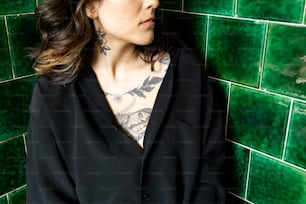 a woman with tattoos standing in front of a green tiled wall