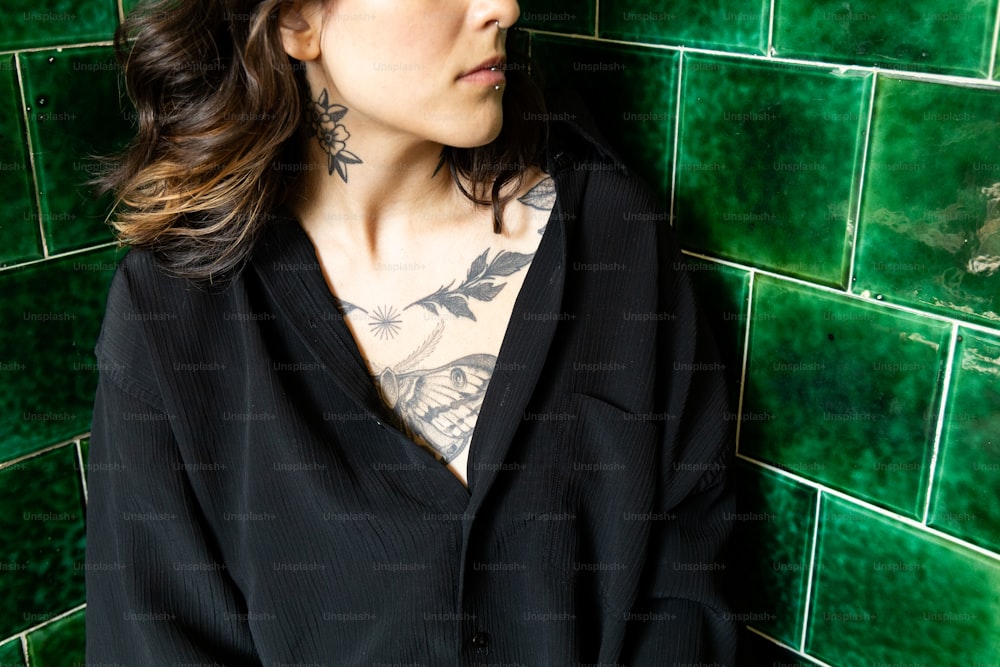 緑のタイル張りの壁の前に立つ刺青の女性