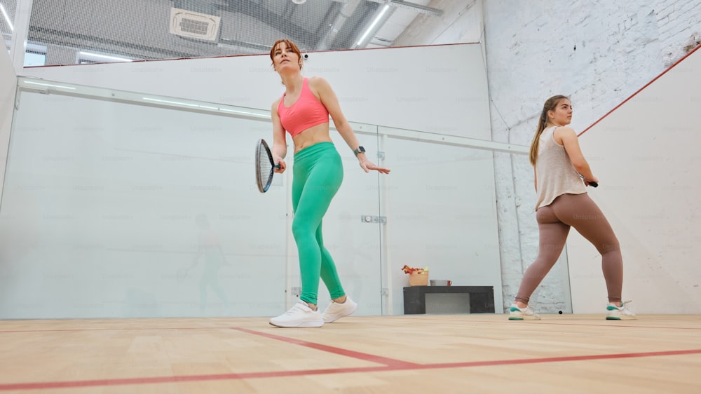 a woman in a pink top and green leggings holding a tennis rac