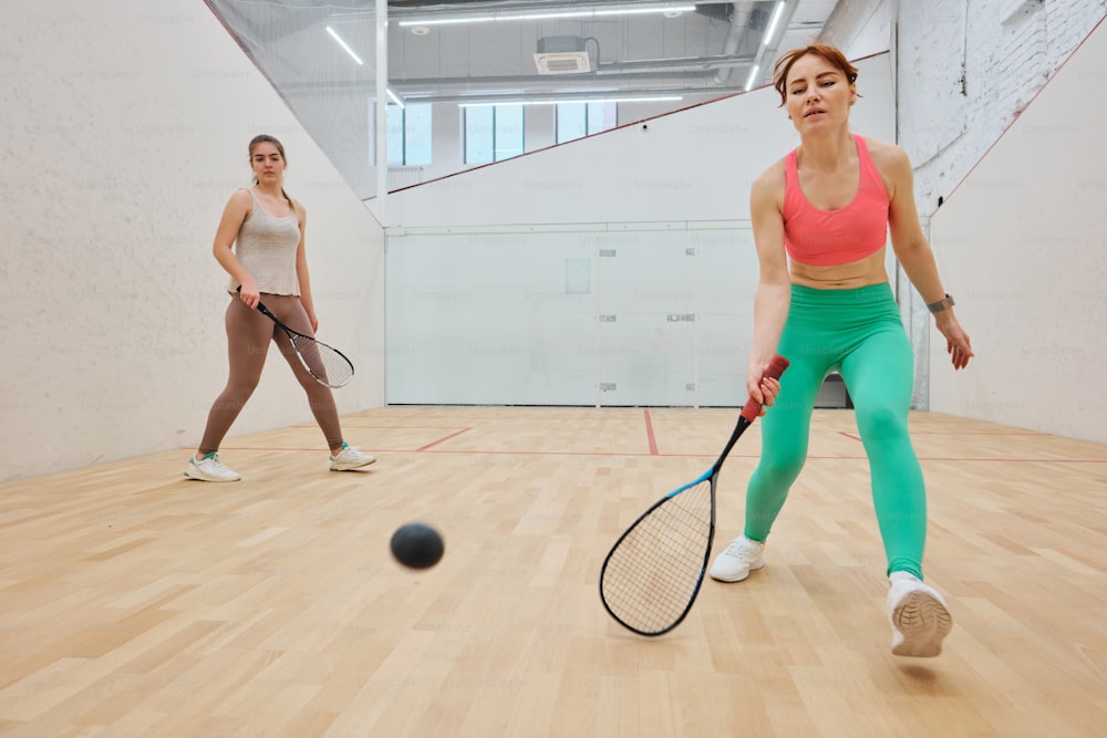 two women are playing tennis on a hard wood floor