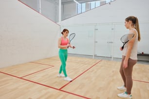 two women standing in a gym holding tennis racquets