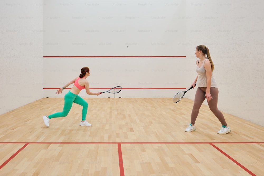 two women playing tennis on a hard wood floor