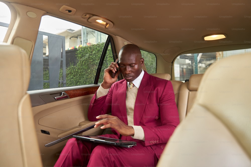 a man in a red suit sitting in a car talking on a cell phone
