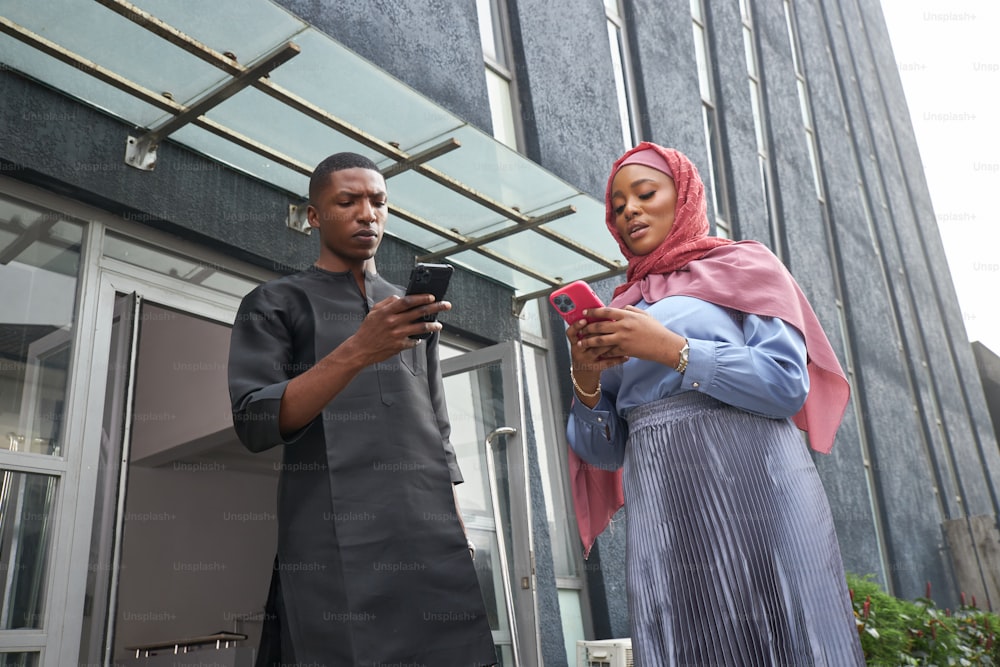 a man and woman standing outside of a building looking at a cell phone