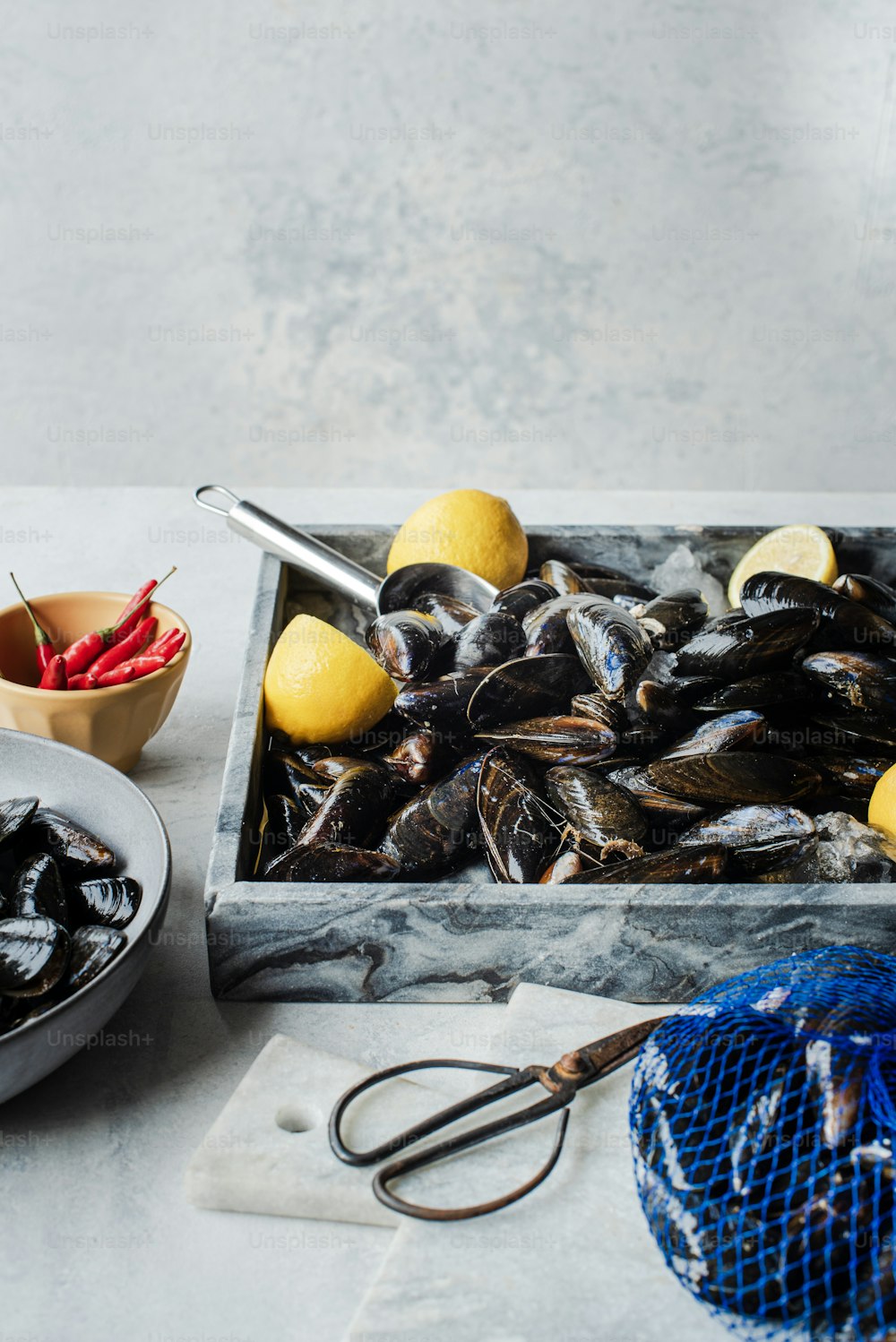 a tray of mussels with lemons and a bowl of chili