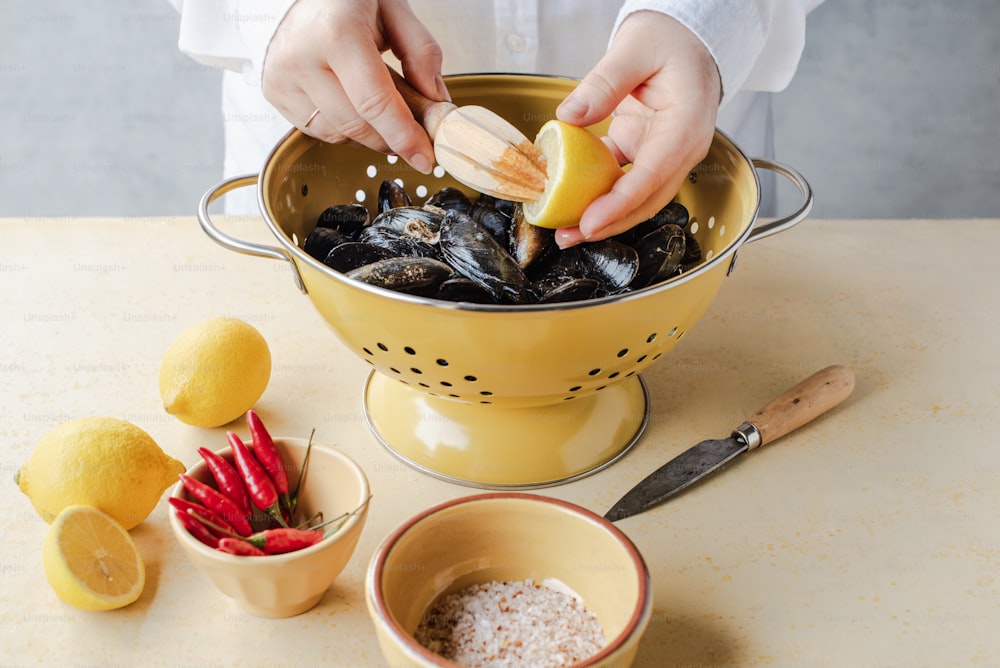 a person is squeezing a lemon into a bowl of mussels